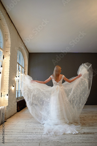 Beautiful lace dress, perfectly sitting on the figure. A beautiful bride stands in a loft-style room, throws up a skirt of a lush wedding dress.