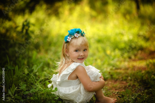 Cute little girl sitting on the lawn in white dress in summer