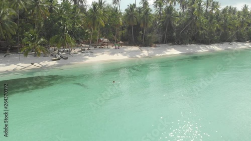 Aerial: flying over woman swimming on turquoise transparent water tropical caribbean sea uncontaminated white sand beach Wab Kei Islands Moluccas Indonesia. Native cinelike D-log color profile photo