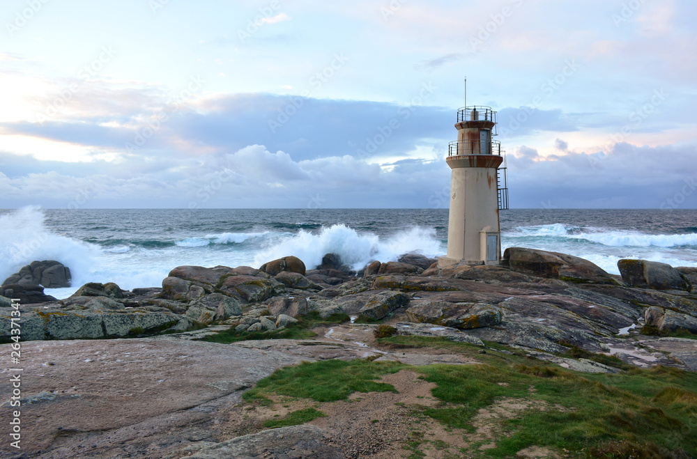 Old lighthouse and waves breaking against the rocks with sunset light. Muxia, Spain.