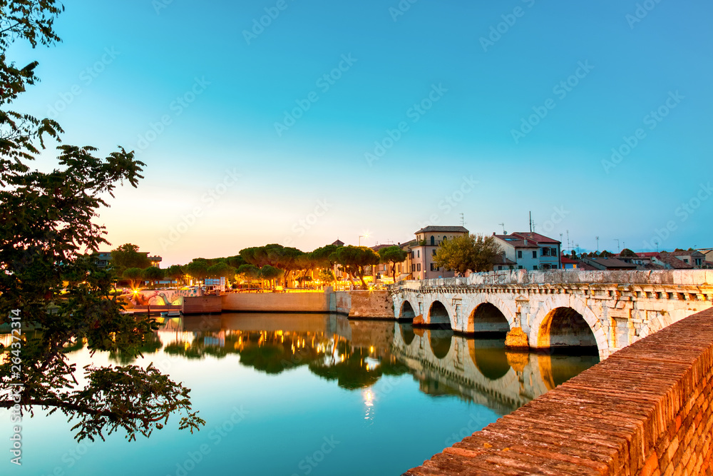 Historical roman Tiberius bridge over Marecchia river during sunset in Rimini, Italy.