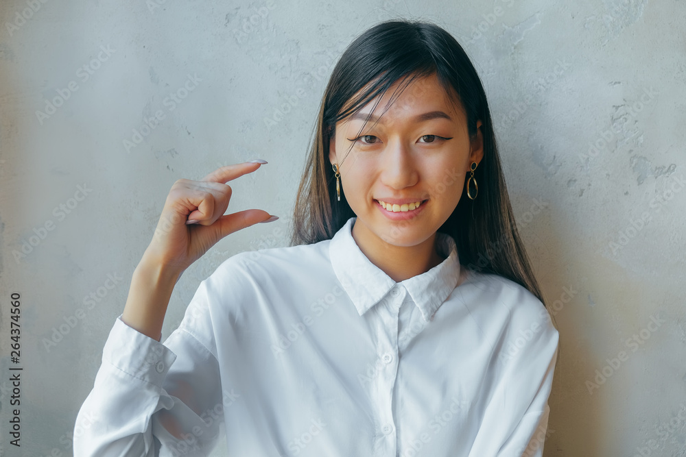 Funny excited asian woman showing something very tiny little size by  fingers, happy girl amazed by small prices looking at camera isolated on  white grey studio background Photos | Adobe Stock