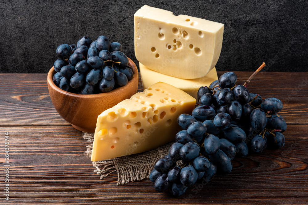 Blue grapes and cheese on dark wooden background.