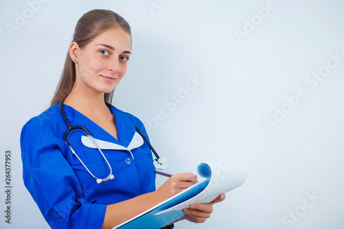 Doctor with a stethoscope, holding a notebook in his hand. Close-up of a female doctor filling up medical form at clipboard while standing straight in hospital photo