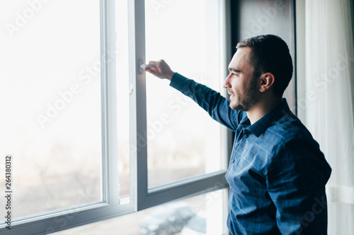 Handsome man is opening the window at home to refresh the room
