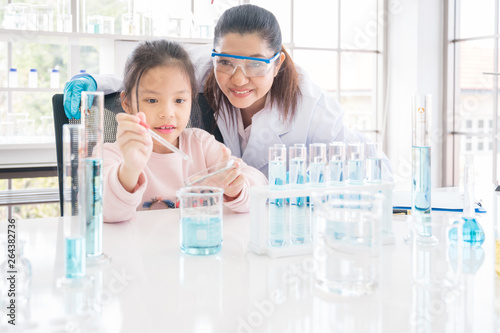 Asian girl school student performing experiment in chemistry lab with scientist teacher