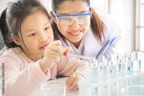 Asian girl school student performing experiment in chemistry lab with scientist teacher