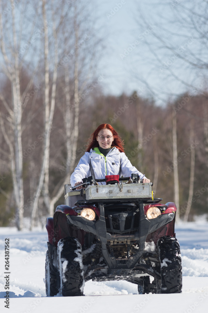 A winter forest. A woman with ginger hair riding big red snowmobile and overcoming the snow