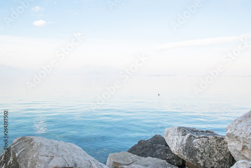 Desenzano del Garda, Italy. Calm beautiful view of italian lake Garda. Amazing landscape in fog with water, sky and mountains. Panorama of gorgeous Lake Garda surrounded by mountains. Heaven on Earth.