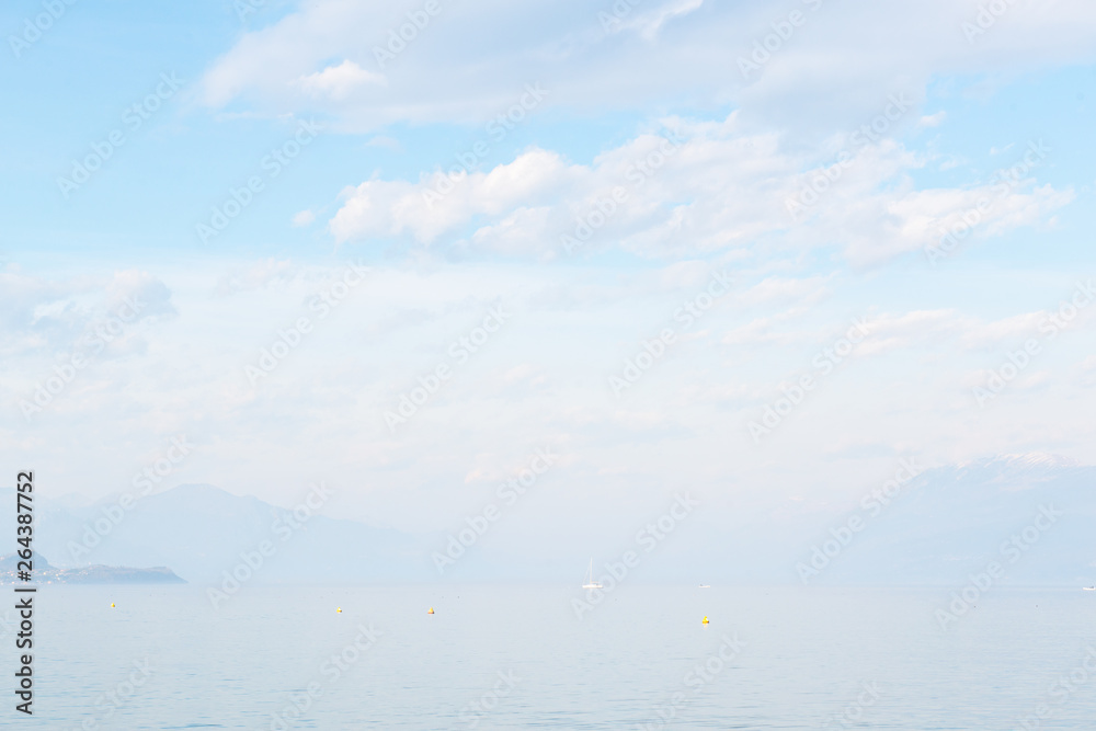 Desenzano del Garda, Italy. Calm beautiful view of italian lake Garda. Amazing landscape in fog with water, sky and mountains. Panorama of gorgeous Lake Garda surrounded by mountains. Heaven on Earth.
