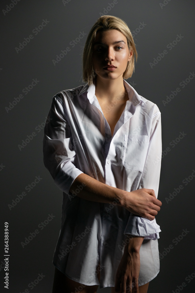 Fashion model. Young blond woman posing in studio wearing white shirt ...