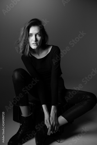 Fashion model. Young woman posing in studio wearing black with boots. Beautiful caucasian girl over gray background. Black and white