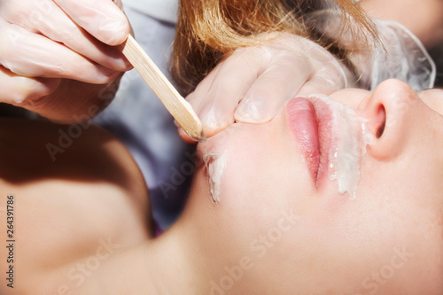 Depilation with hot wax mustache in the beauty salon. Young woman receiving facial epilation close up. Cosmetologist removes hair on face. Beauty salon, mustache depilation photo