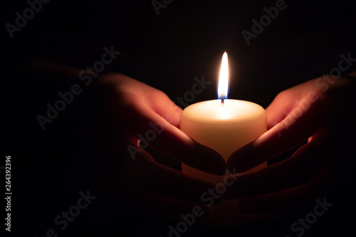 Female hand holding a burning candle in the dark