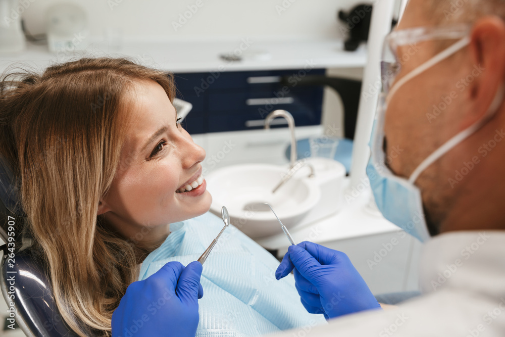 Image of caucasian woman sitting in dental chair while professional doctor fixing her teeth Image of caucasian woman sitting in dental chair while professional doctor fixing her teeth