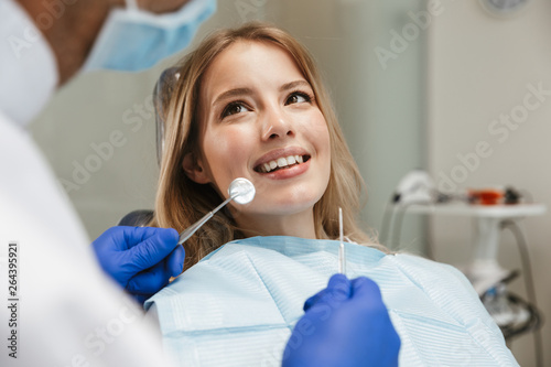 Image of smiling woman sitting in dental chair while professional doctor fixing her teeth
