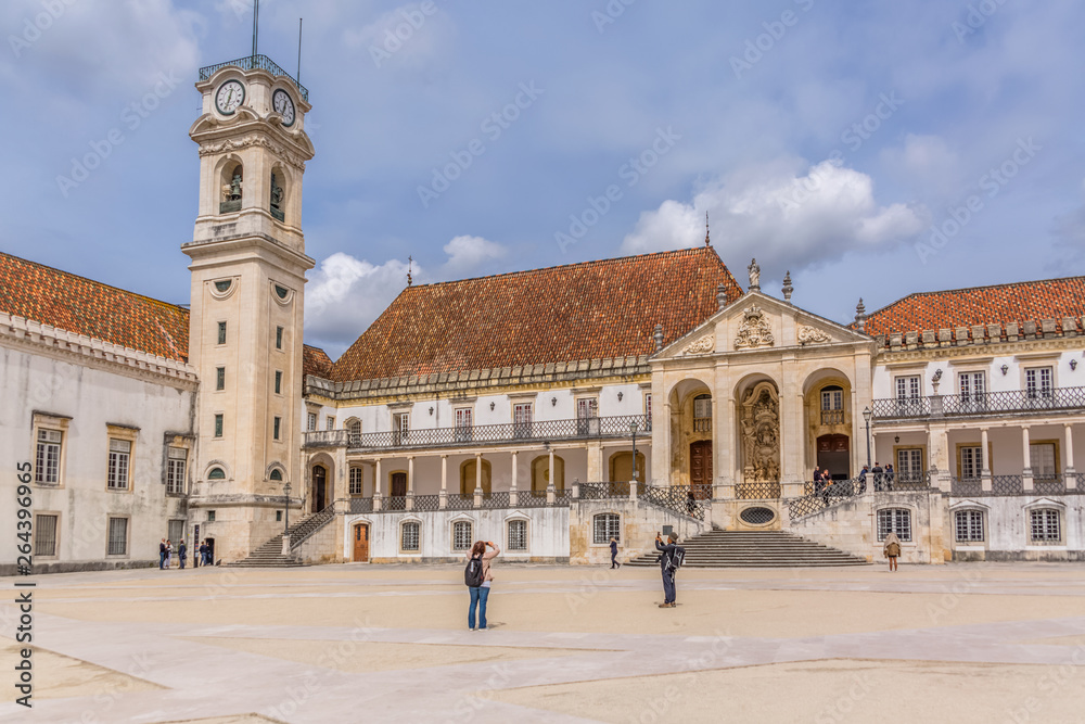 View of the tower building of the University of Coimbra, classic architectural structure with masonr and other classic buildings around, tourists in scene, in Coimbra, Portugal