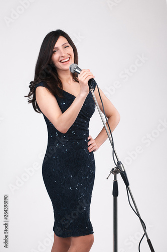 beautiful young girl in a dress holding a microphone in her hands, singing, smiling, looking into the camera. on a white background