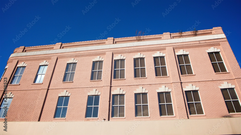 The facade of a small town mid-century designed building painted in pink against a clear blue sky in horizontal image format.