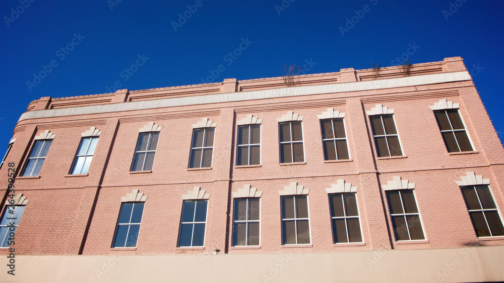 The facade of a small town mid-century designed building painted in pink against a clear blue sky in horizontal image format.