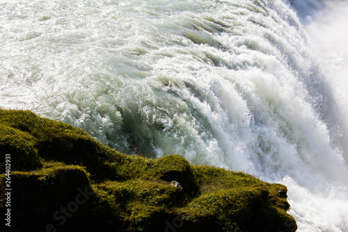 Powerful flows of water from the giant and fierce Gullfoss waterfall, tons of water breaking down from the rocks in Iceland. Powerful and mighty icelandic nature. Green moss, stones on the foreground.