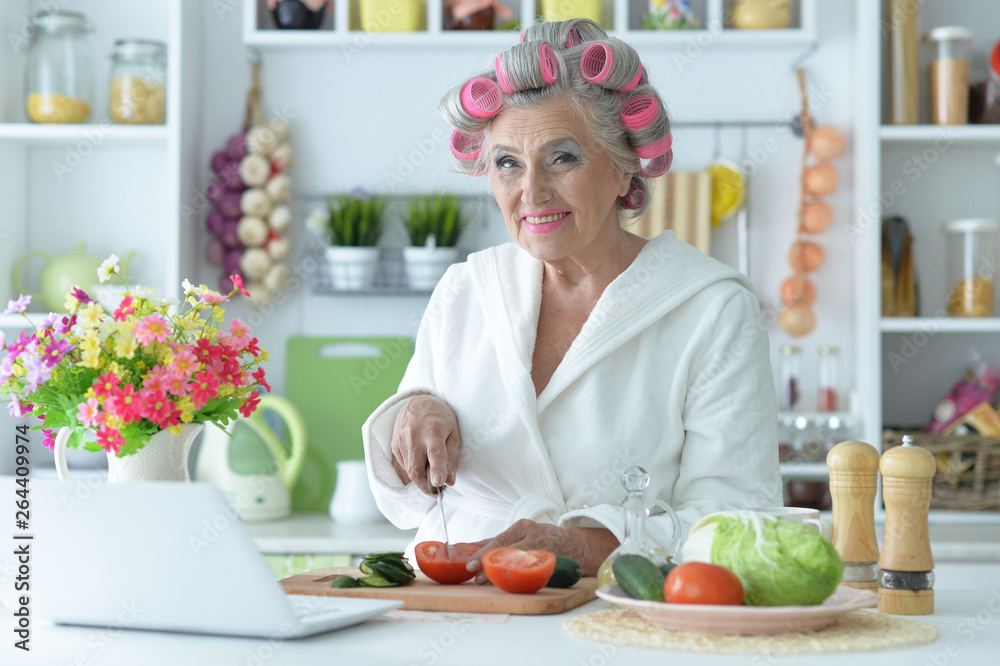 Portrait of senior woman in hair rollers cutting vegetables on kitchen table Portrait of senior woman in hair rollers cutting vegetables on kitchen table
