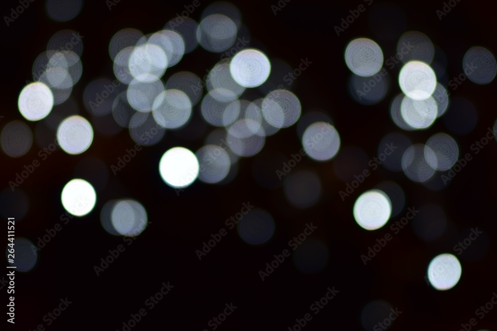 Small white bokeh balls from festive city lights on a contrasting black background