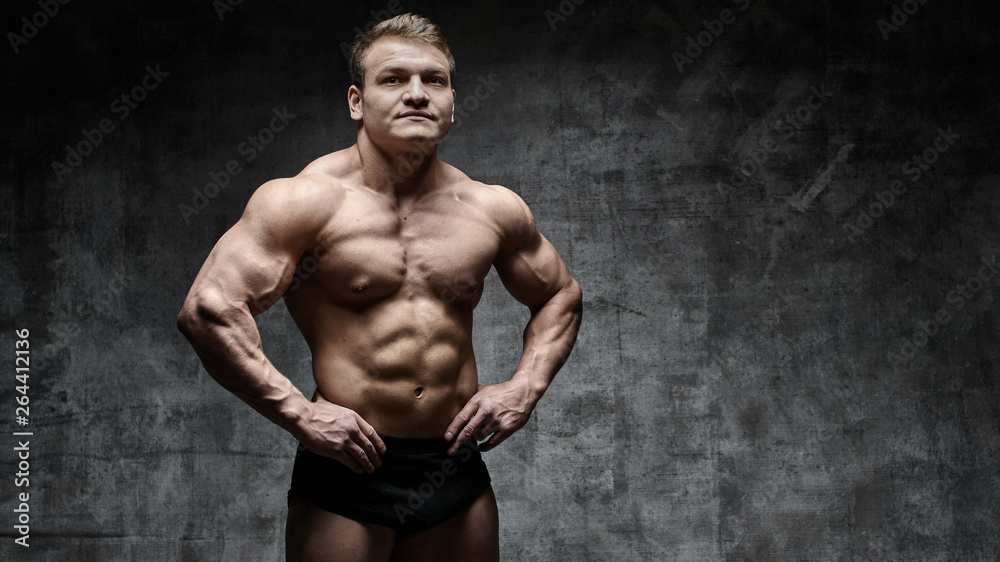 Sexy bodybuilder man posing on dark background in black shorts. Handsome pumped male body isolated with free space for advertising