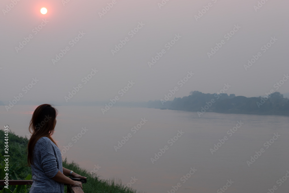 Women standing on the balcony watching the sunset by the river, Women standing by the river, A young woman stood on the bank of the river in the evening with the sun going down