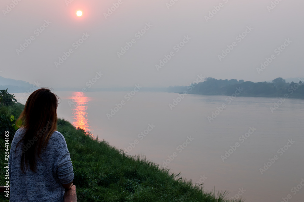 Women standing on the balcony watching the sunset by the river, Women standing by the river, A young woman stood on the bank of the river in the evening with the sun going down