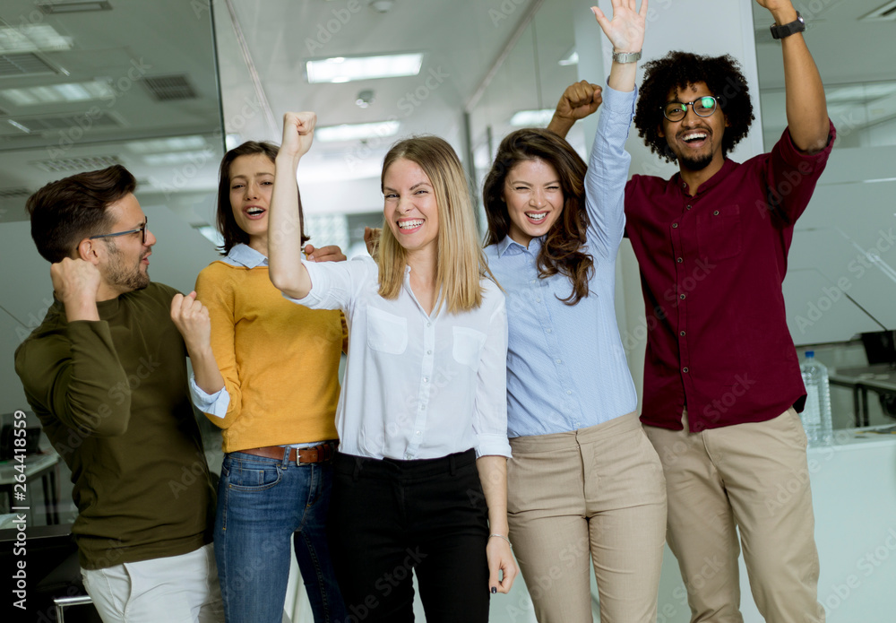 Obraz premium Group of young excited business people with hands up standing in office