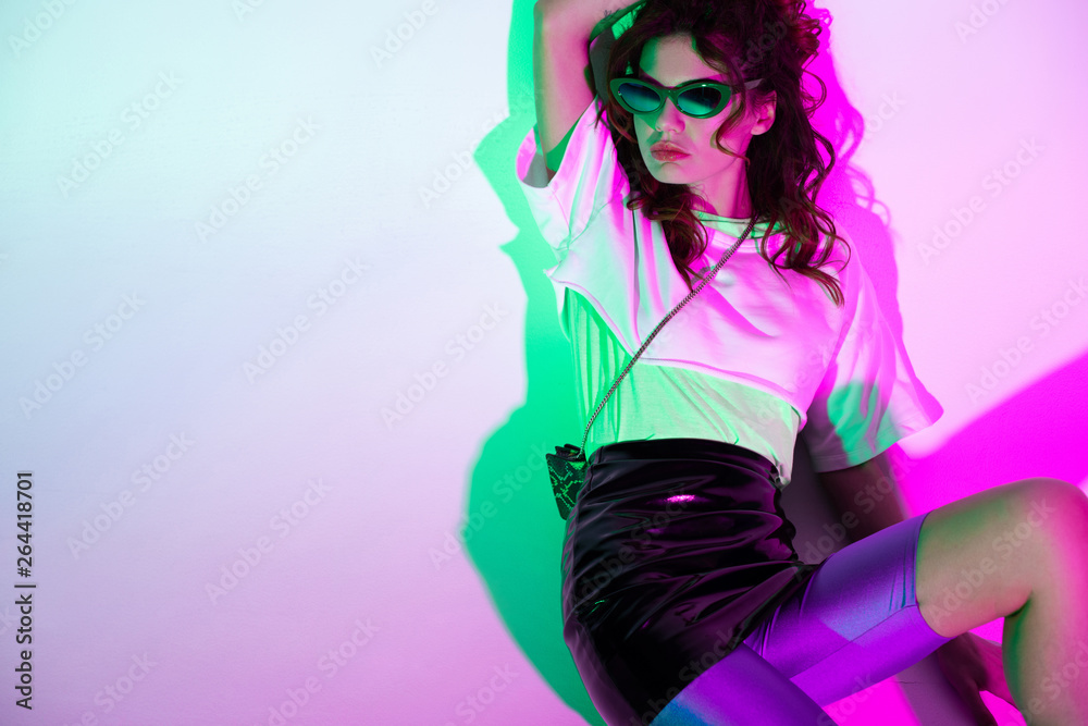 trendy and beautiful young woman in sunglasses sitting on purple with gradient