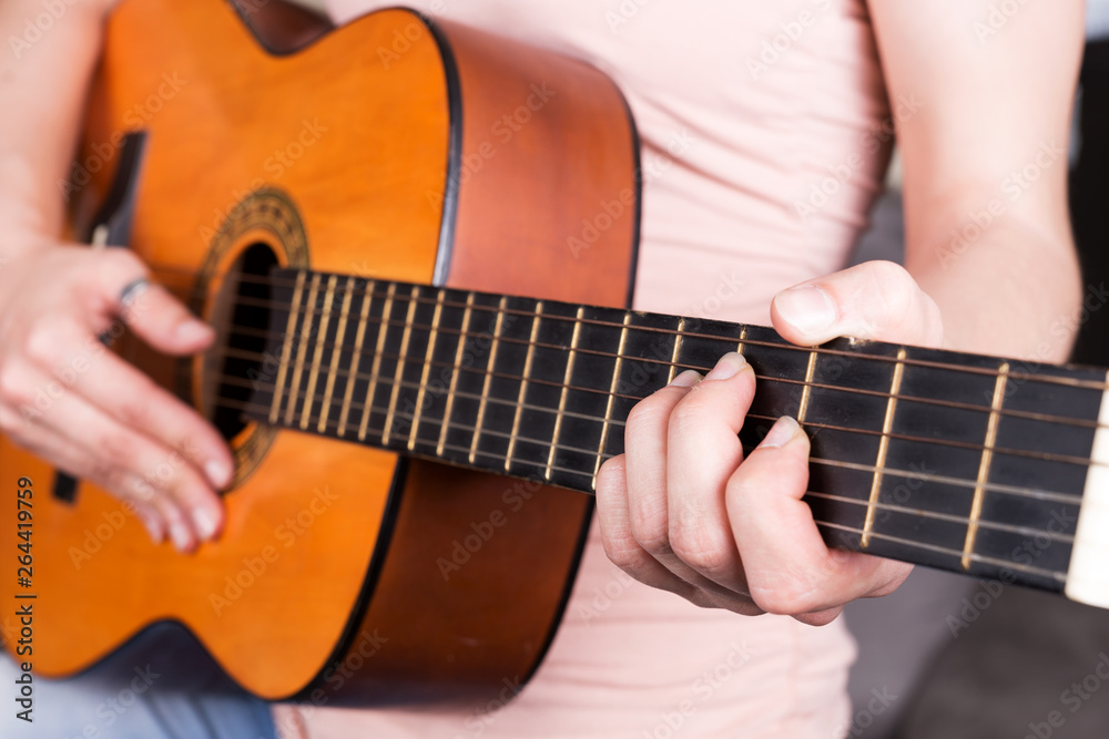 Fototapeta premium Closeup of young woman hand playing acoustic guitar. Teen girl learning to play song