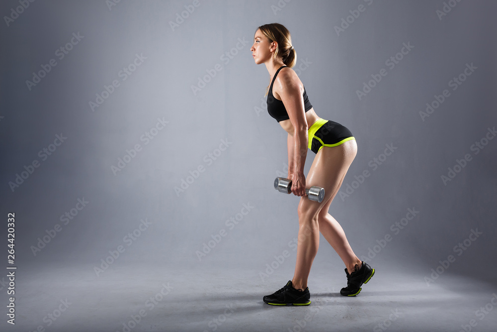 Strong young sportswoman trains with dumbbells in a sport suit. Concept of pumping muscle and nutrition. Copyspace