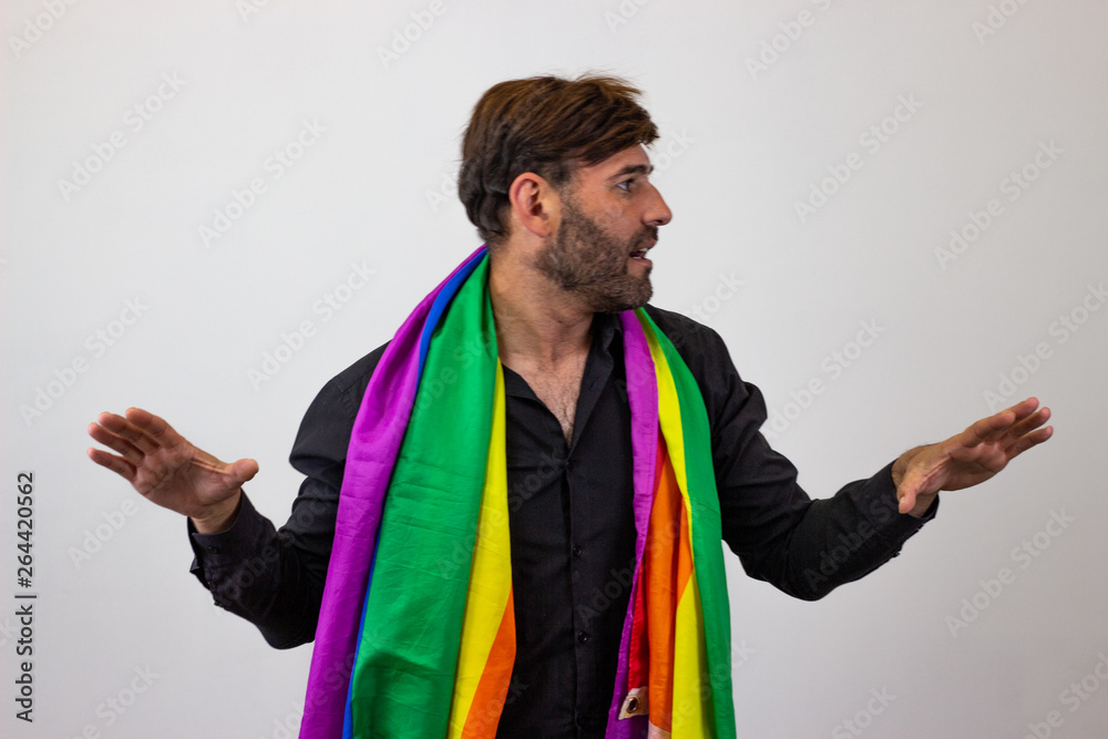 Portrait of handsome young man with gay pride movement LGBT Rainbow flag and brown hair holding up one finger, facing forwards and looking at the side. Isolated on white background.