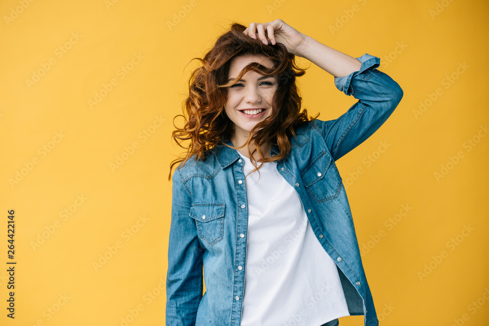 pretty young cheerful woman touching hair and smiling on orange pretty young cheerful woman touching hair and smiling on orange
