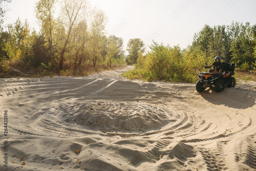 Fototapeta premium Atv rider in helmet climbing sandy road in forest