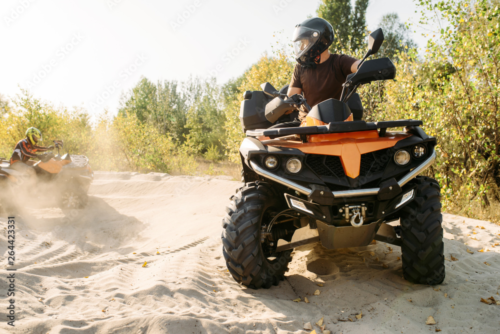 Fototapeta premium Two atv riders in helmets ride in a circle on sand