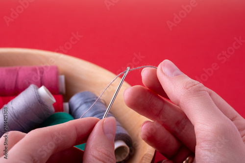 Thread into needle process woman hands on red background