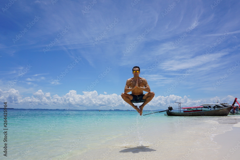 Fit and active Asian man jumping whilst on the beach with crystal clear waters in Thailand island vacation meditation spiritual relaxing lift off