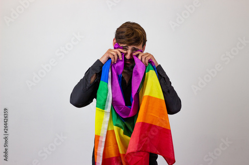 Portrait of handsome young man with gay pride movement LGBT Rainbow flag and brown hair unhappy, looking at the camera. Isolated on white background.