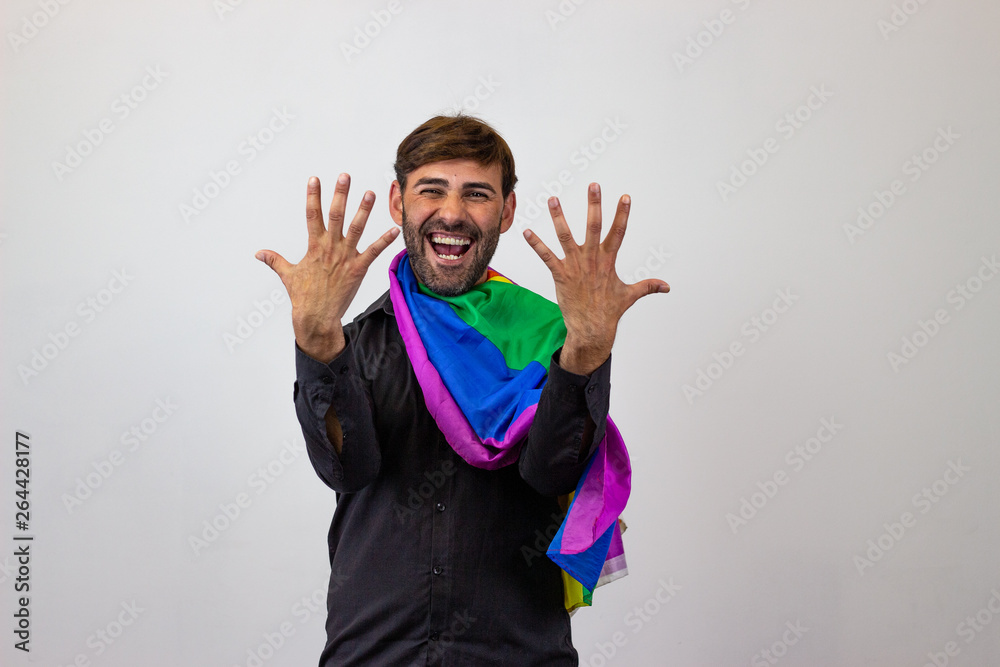 Portrait of handsome young man with gay pride movement LGBT Rainbow flag and brown hair pointing while laughing, looking at the camera. Isolated on white background. Portrait of handsome young man with gay pride movement LGBT Rainbow flag and brown hair pointing while laughing, looking at the camera. Isolated on white background.