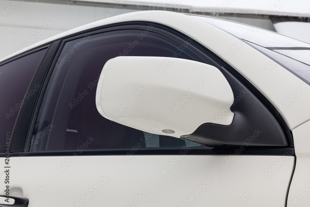 Close-up of the side left mirror with turn signal repeater and window of the car body white SUV on the street parking after washing and detailing in auto service industry. Road safety while driving