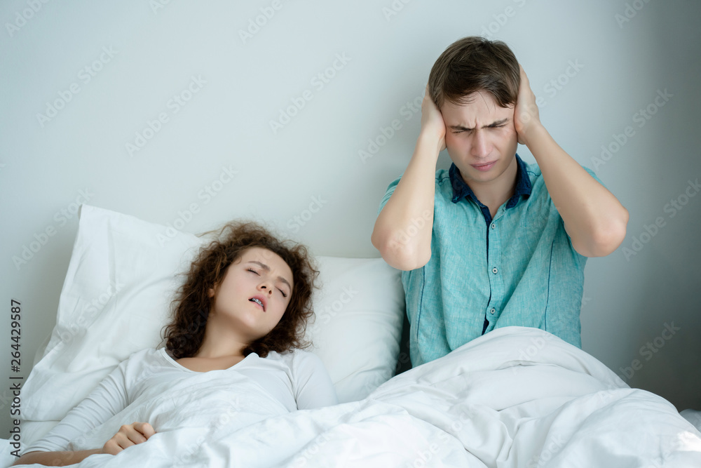 Caucasian Couple on bed with white mattress woman snoring loud makes man feel annoyed. Causes