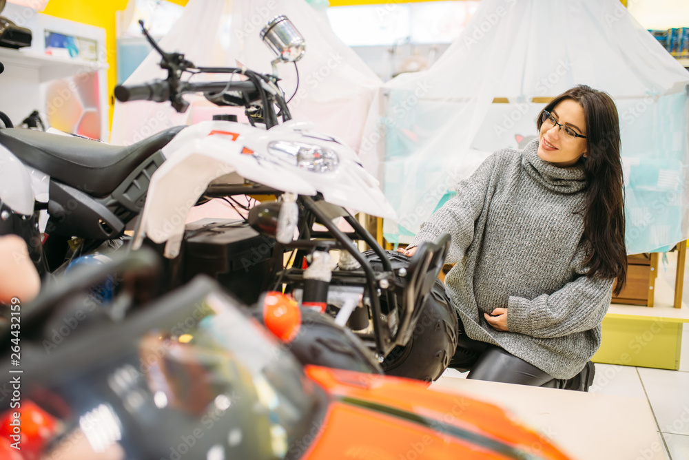 Pregnant woman choosing electric car in toy store Pregnant woman choosing electric car in toy store