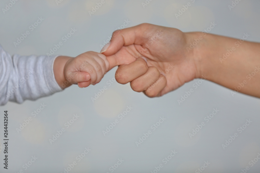Obraz premium Little baby holding mother's finger on light background, closeup