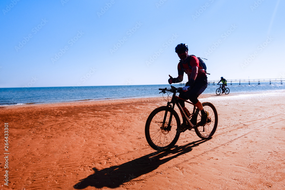 Man cycling on sport bike showing thumb up on ocean background - Silhouette of people riding bicycle on the beach shore with morning backlight - Lifestyle concept of healthy holiday activity - image Man cycling on sport bike showing thumb up on ocean background - Silhouette of people riding bicycle on the beach shore with morning backlight - Lifestyle concept of healthy holiday activity - image