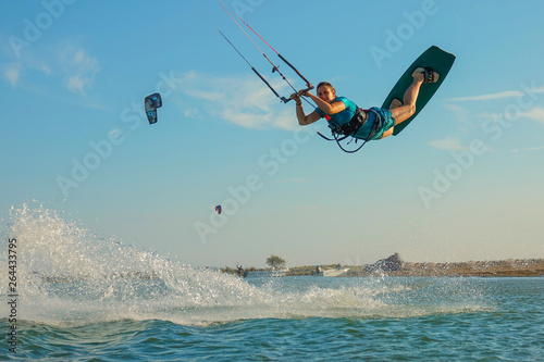 LOW ANGLE: Happy young woman jumps high in the air while kiteboarding in Greece. © helivideo