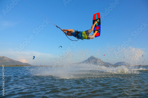 Young male tourist jumping and doing tricks while kitesurfing in sunny Greece.