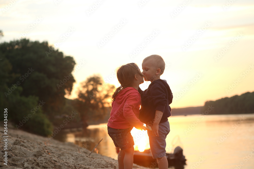 children boy and girl kiss sunset river